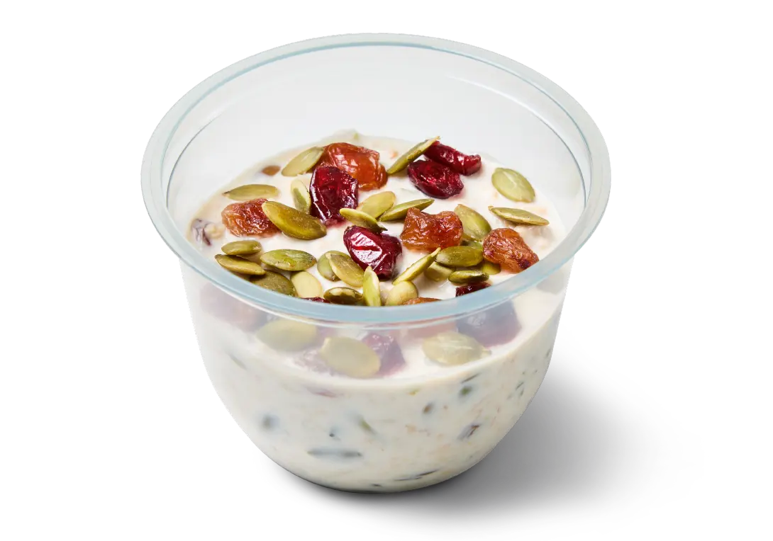 Overnight Oats with Seeds & Dried Fruit from the Greggs menu in a clear pot topped with pumpkin seeds and dried fruit.